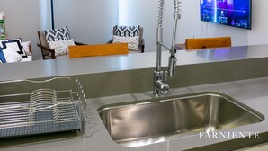 A modern kitchen with a stainless steel sink, a dish rack, and a flat-screen TV mounted on the wall.