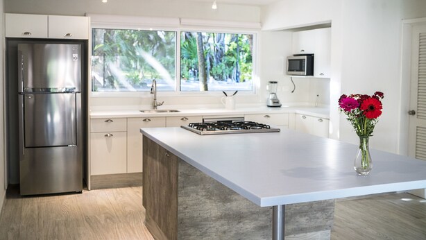 A modern kitchen with a stainless steel refrigerator, a gas stove, and a large window with a view of greenery. - Casa Matuk 3 Refurnished Home Excelent for Family Retreat (Playa del Carmen)
