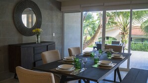 A dining area with a dark wooden table set for four, surrounded by beige upholstered chairs. A large mirror hangs on the wall above the table, and a vase with yellow flowers is placed on a dark wooden console. - Casa Matuk 3 Refurnished Home Excelent for Family Retreat (Playa del Carmen)