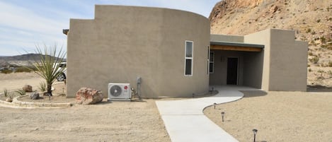A modern building with a curved facade, an air conditioning unit, and a paved driveway leading to the entrance.