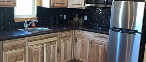 Una cocina con armarios de madera, un refrigerador de acero inoxidable, un microondas y un fregadero.