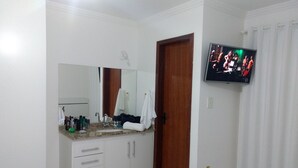 A hotel room with a bathroom vanity, a television mounted on the wall, and a bed with white bedding. - Casa 13 Condomínio Mont Moriá (Porto Seguro)
