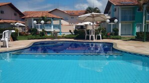 En swimmingpool med flisekanter, omgivet af hvide liggestole og parasoller.
