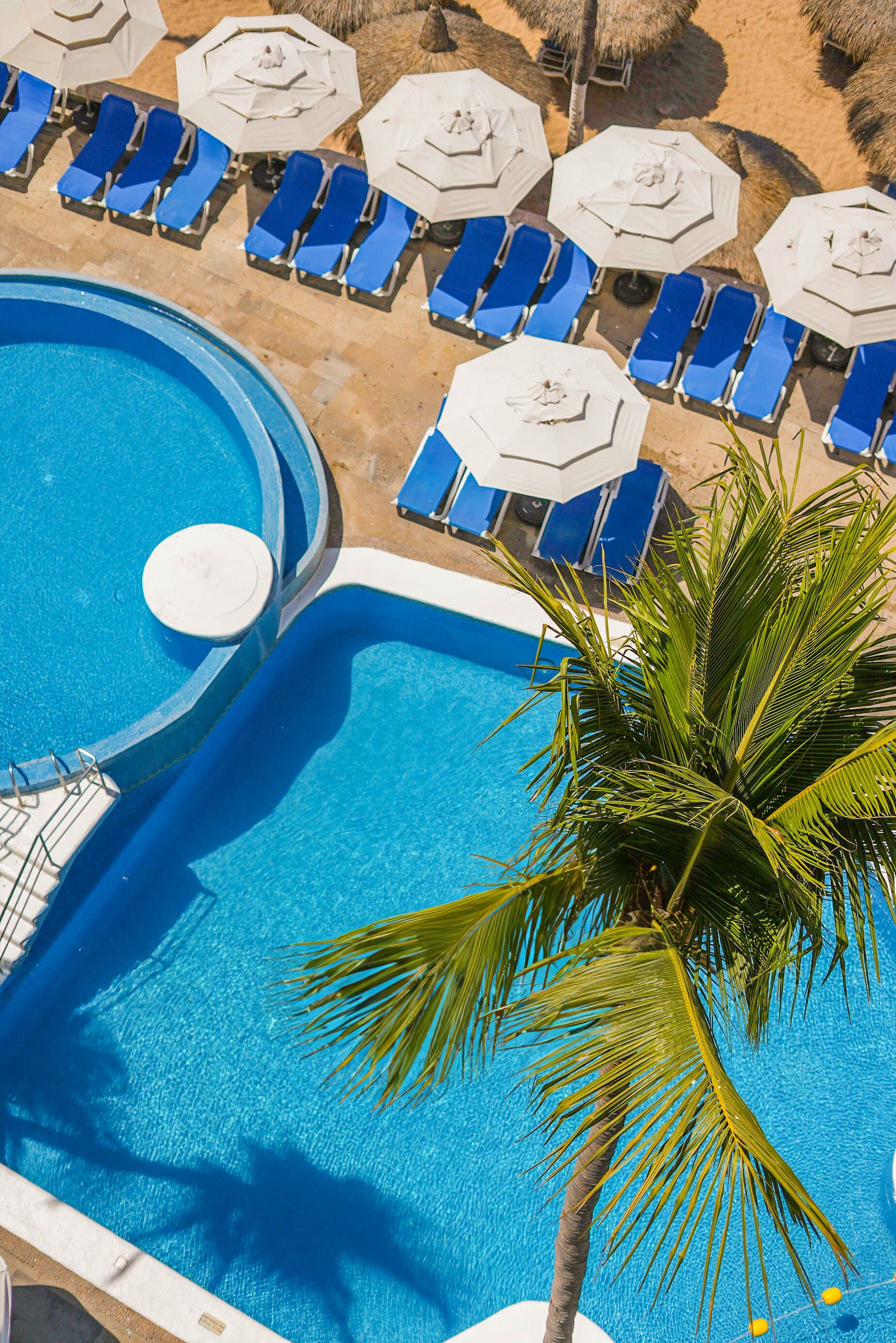 A pool area with blue lounge chairs and white umbrellas.
