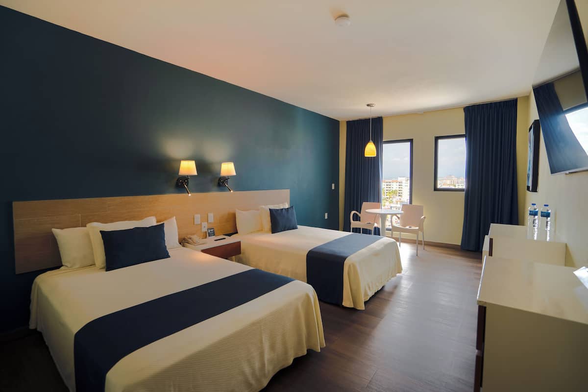 A hotel room with two beds, a desk, and a chair.