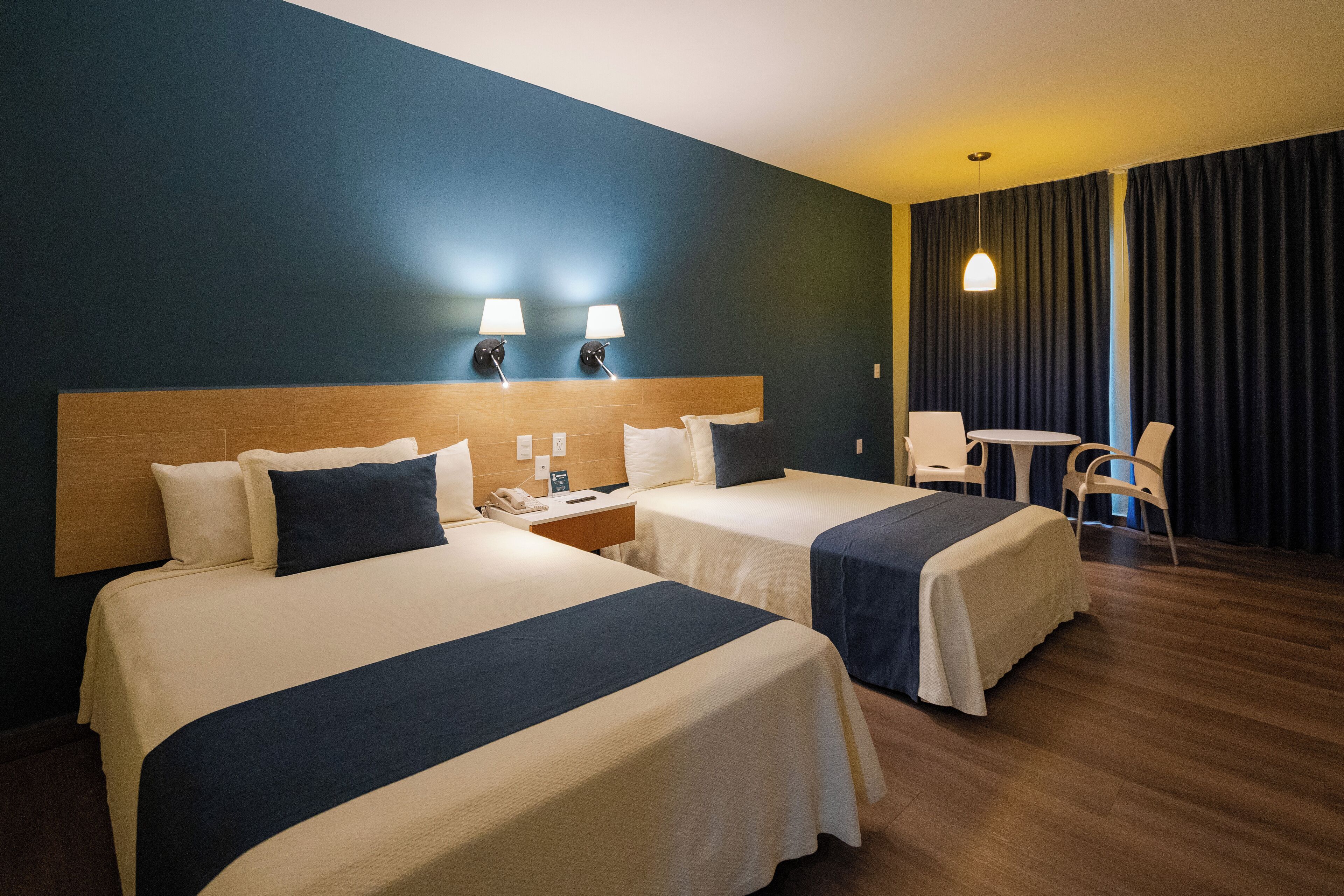 A hotel room with two beds, a small table, a chair, and a lamp.
