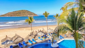 A poolside area with lounge chairs and umbrellas, overlooking a beach and ocean. - Oceano Palace Beach Resort (Mazatlán)