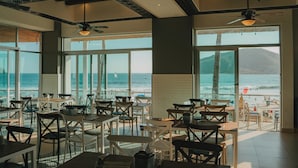 A restaurant with large windows offering ocean views, ceiling fans, and a mix of table and chair arrangements. - Oceano Palace Beach Resort (Mazatlán)