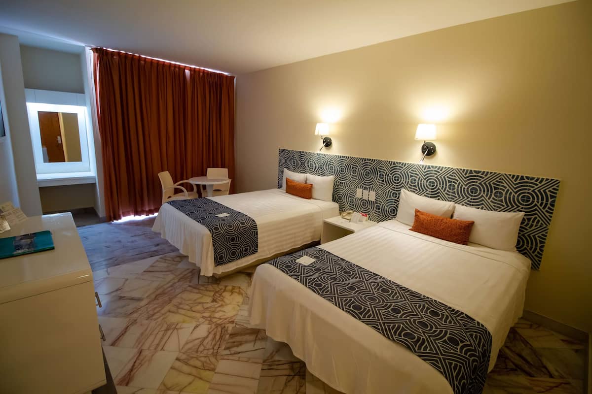 A hotel room with two beds, a desk, a chair, and a window with curtains.