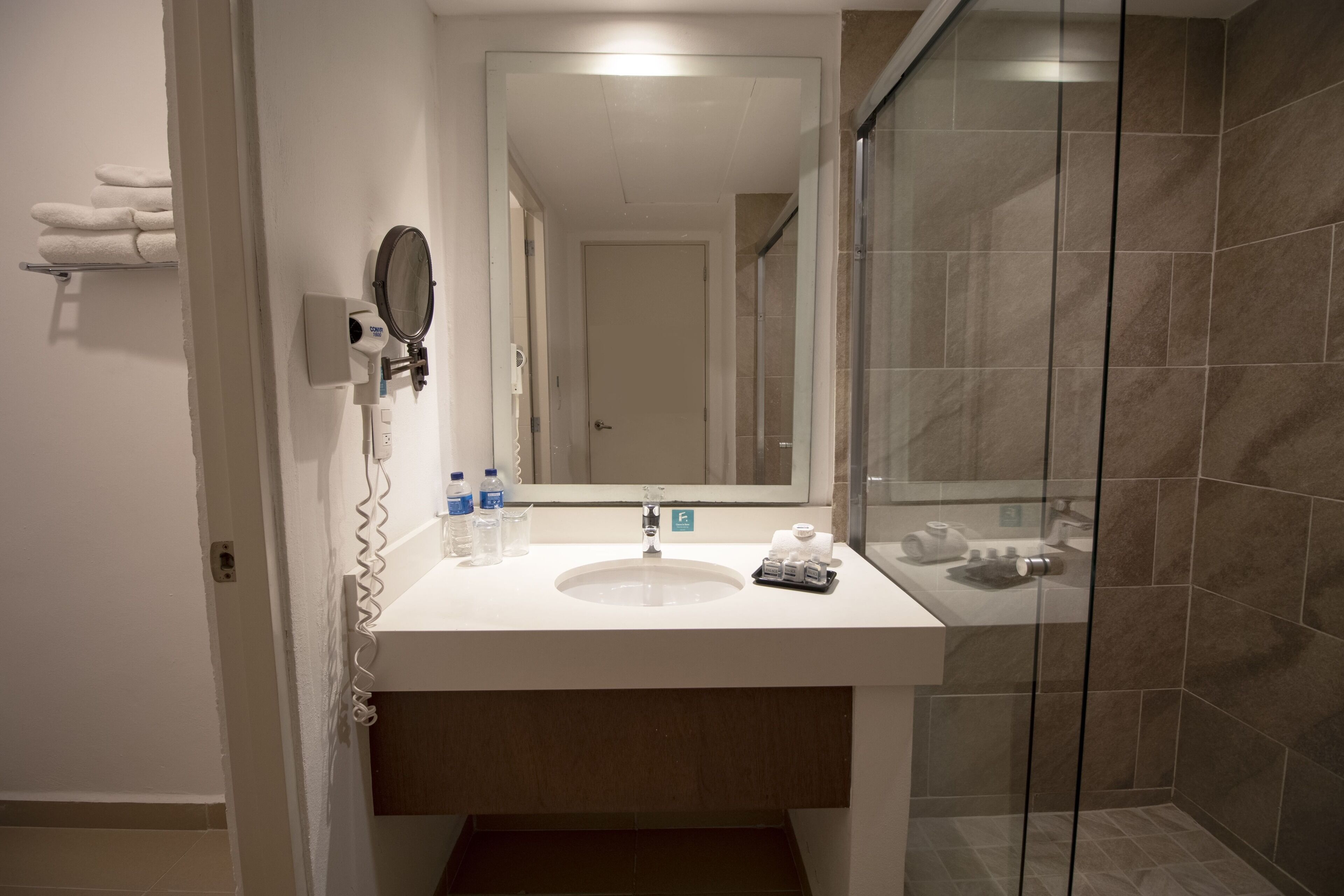 A bathroom with a white sink, a mirror, a glass shower enclosure, and a towel rack with towels.