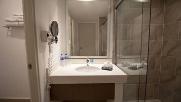 A bathroom with a white sink, a mirror, a glass shower enclosure, and a towel rack with towels.