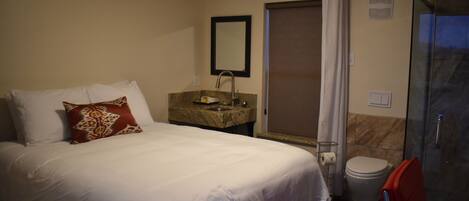 A hotel room with a bed, a bathroom with a shower, and a toilet.