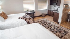 A bedroom with two beds, a small table, and a kitchen area with cabinets and a sink. - Iron Springs Adventure Resort & RV Park (Cedar City)