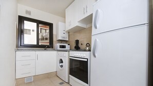 Une cuisine de taille réduite, dotée d’appareils électroménagers blancs, notamment un four à micro-ondes, un four traditionnel et un lave-linge.