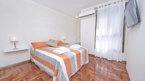 A double bed with striped bedding, a bedside table with a lamp, and a wall-mounted TV. - Pueyrredón R7E (Córdoba)
