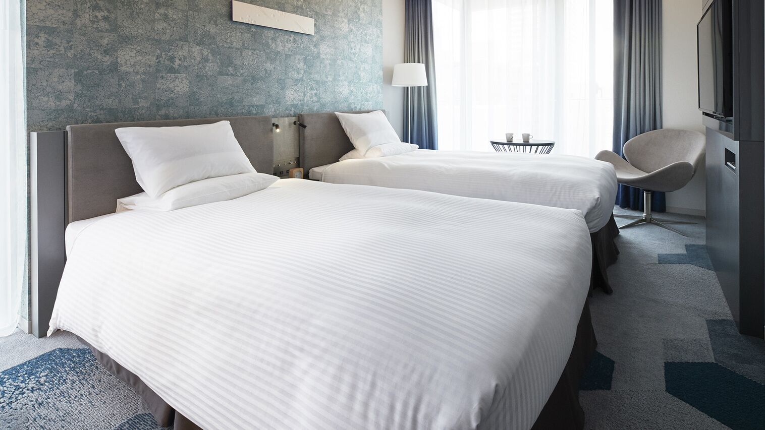 Ein Hotelzimmer mit zwei Betten, einem Sessel, einem kleinen Tisch mit Tassen und Blick ins Freie.