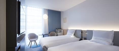 A hotel room with two beds, a desk, a chair, a lamp, and a window with curtains.