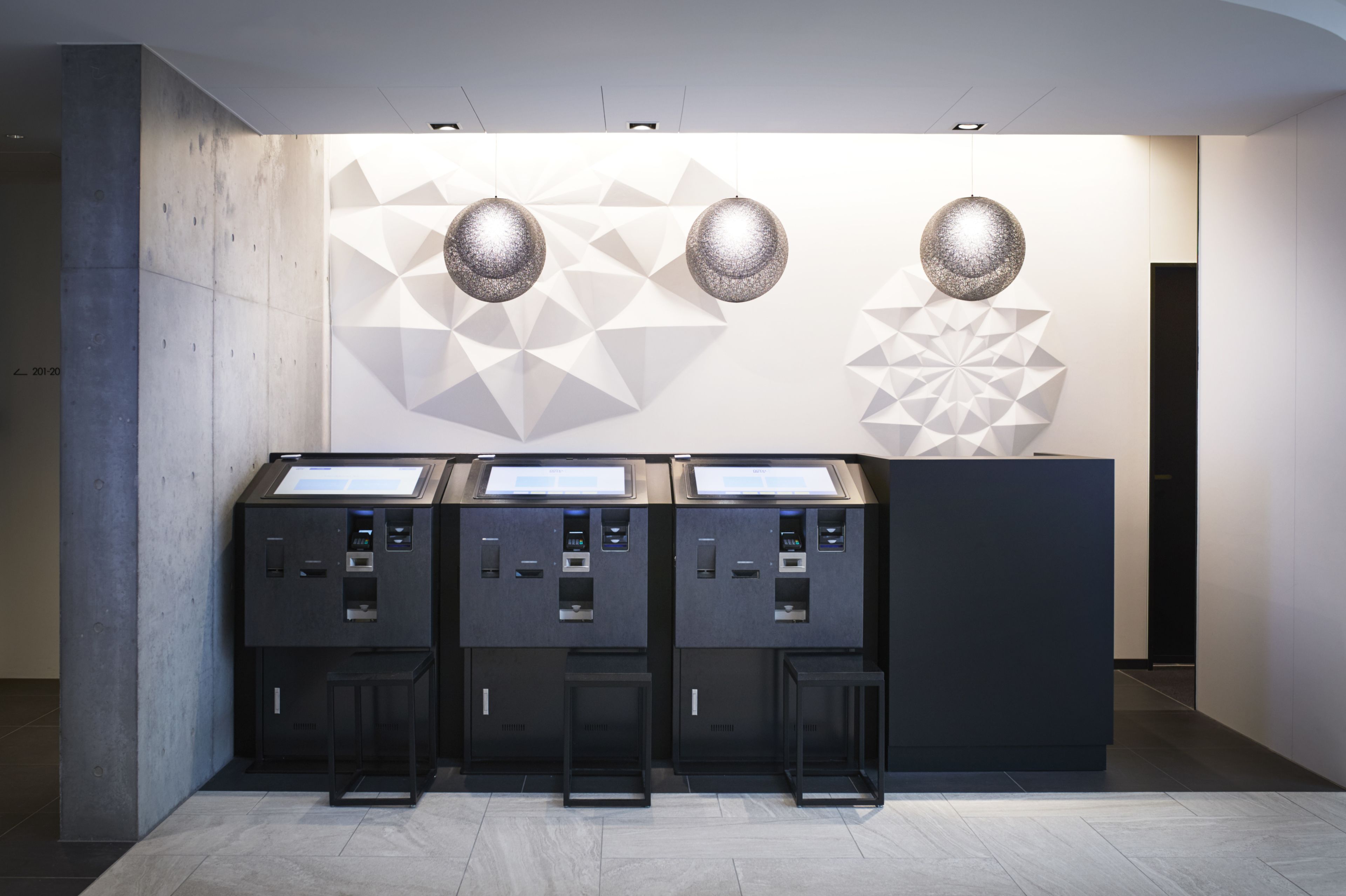 A modern kiosk with three interactive screens, geometric wall art, and hanging spherical lights.