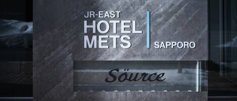 A modern hotel sign with "JR-EAST HOTEL METS SAPPORO" and "Source" written on it.