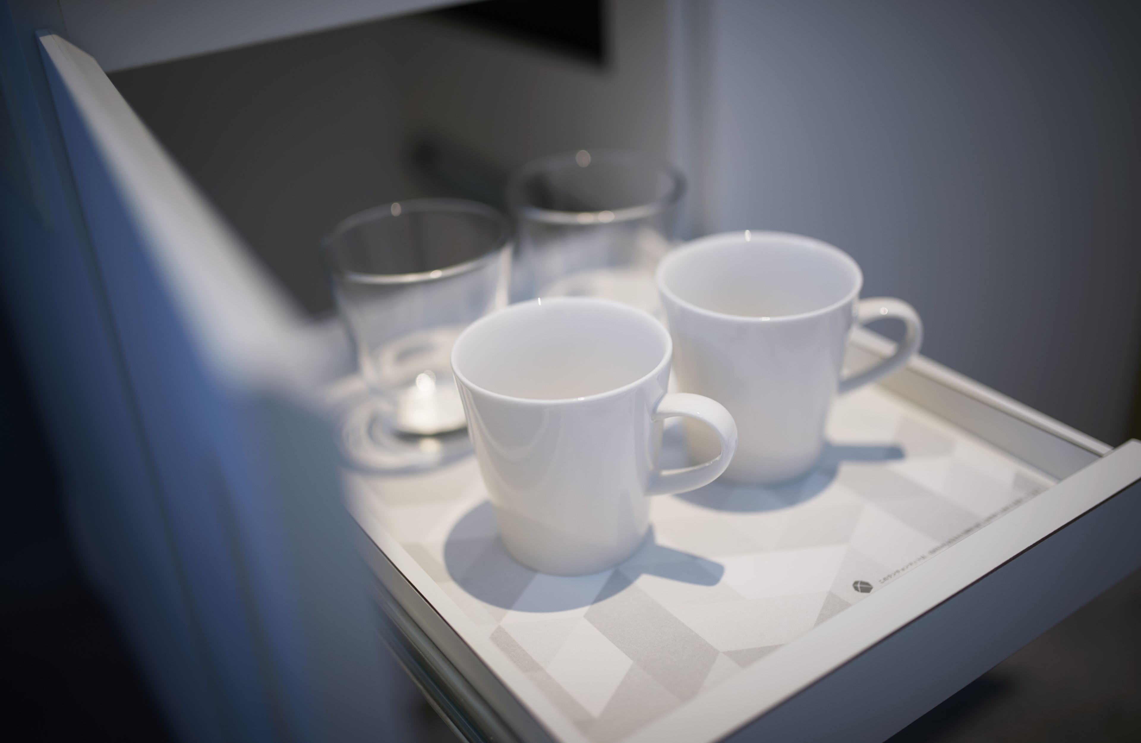 A tray with three white mugs and two clear glasses on a white tray.