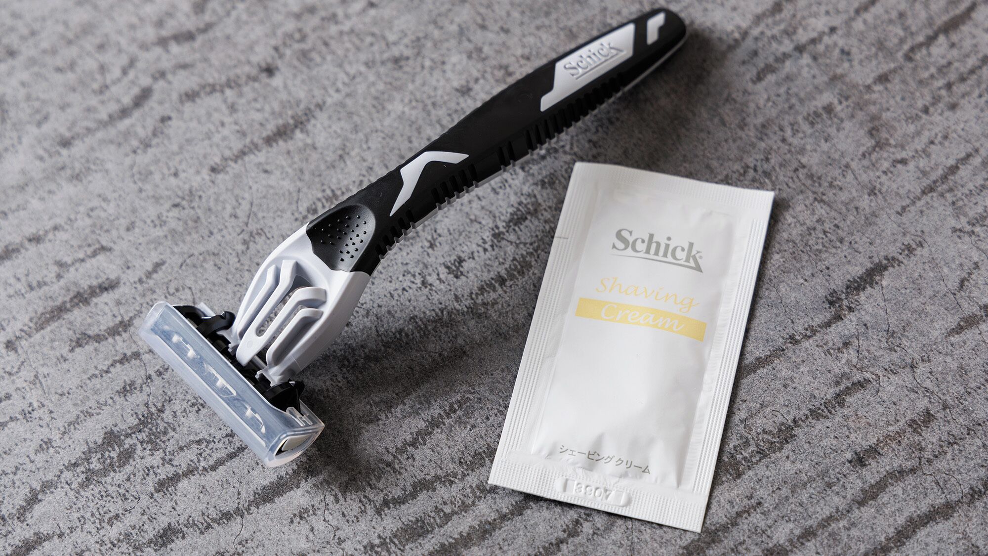 A Schick razor and a tube of shaving cream on a textured surface.