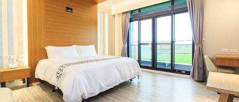 Quarto de hotel moderno com uma cama grande, teto de madeira e vista para uma paisagem verde através de uma janela ampla.
