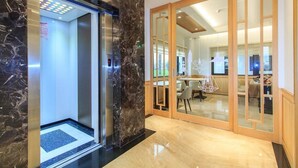 A modern hotel lobby with a marble floor, an elevator, and a glass partition leading to a dining area. - Urban Oasis Inn (Luodong)