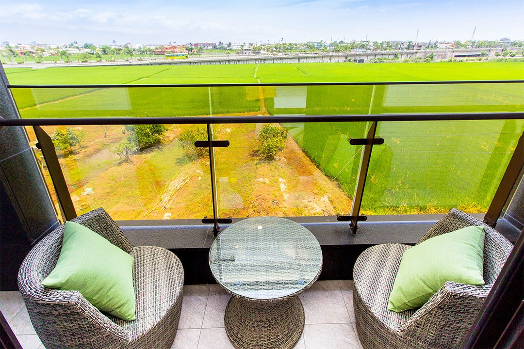 Un balcon doté de meubles en osier et d’une table en verre, donnant sur un champ verdoyant.