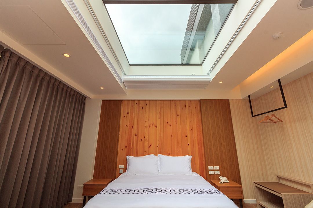 Habitación de hotel con tragaluz, paredes de paneles de madera, una cama con ropa blanca, una mesita de noche con teléfono y un escritorio.