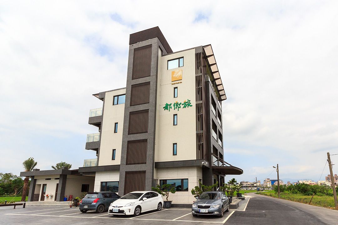 A multi-story hotel with a modern design, featuring a prominent entrance and a parking area with several cars.