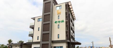 A multi-story hotel with a modern design, featuring a prominent entrance and a parking area with several cars.