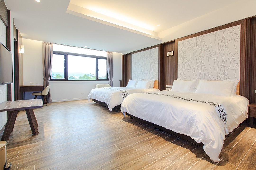 A hotel room with two beds, a desk, and a large window.