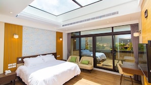 A modern hotel room with a large bed, two armchairs, a desk, and a large window offering a city view. - Urban Oasis Inn (Luodong)