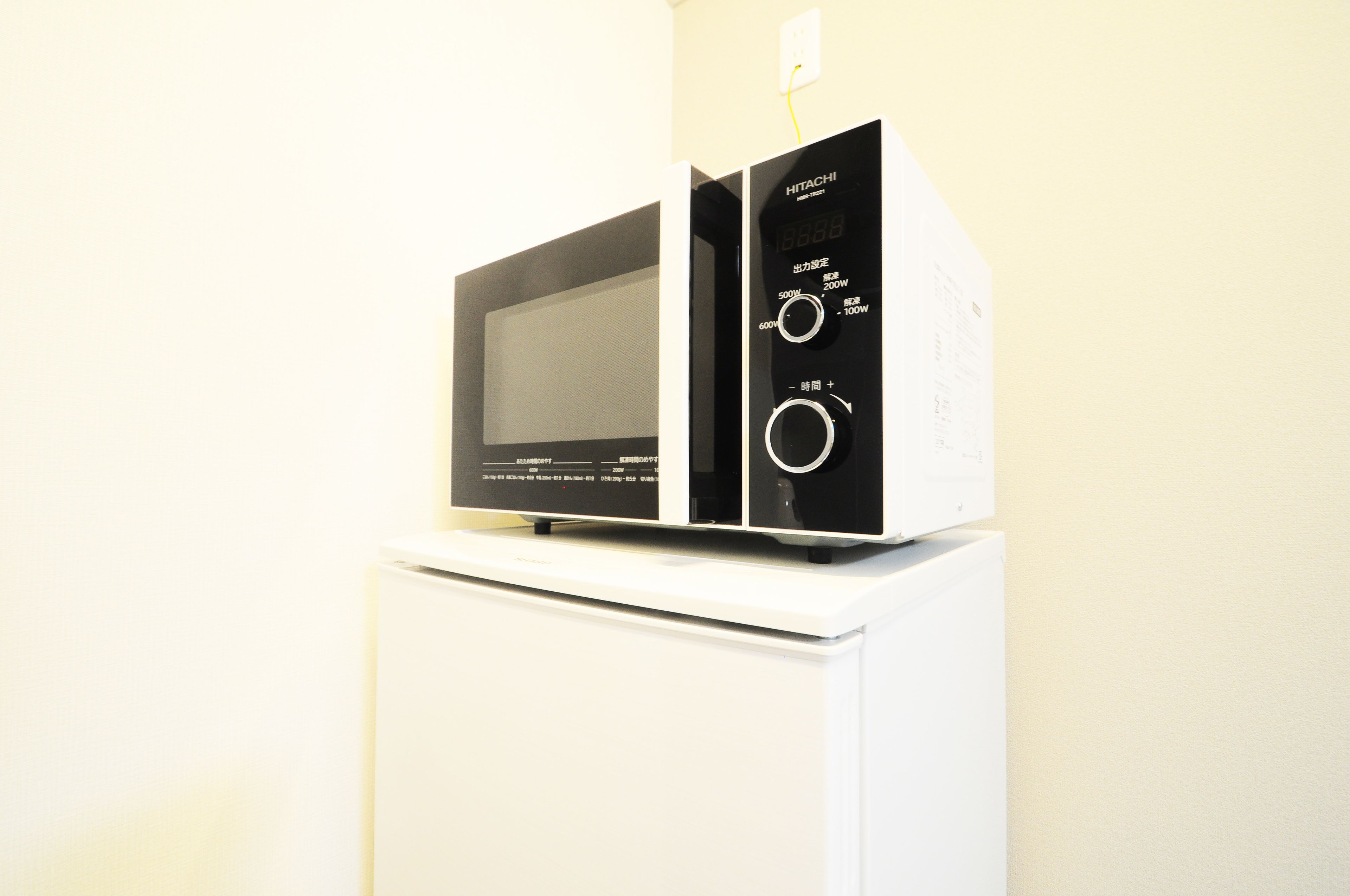 Un horno microondas sobre un electrodoméstico blanco, posiblemente un refrigerador, con pantalla digital y perillas de control.