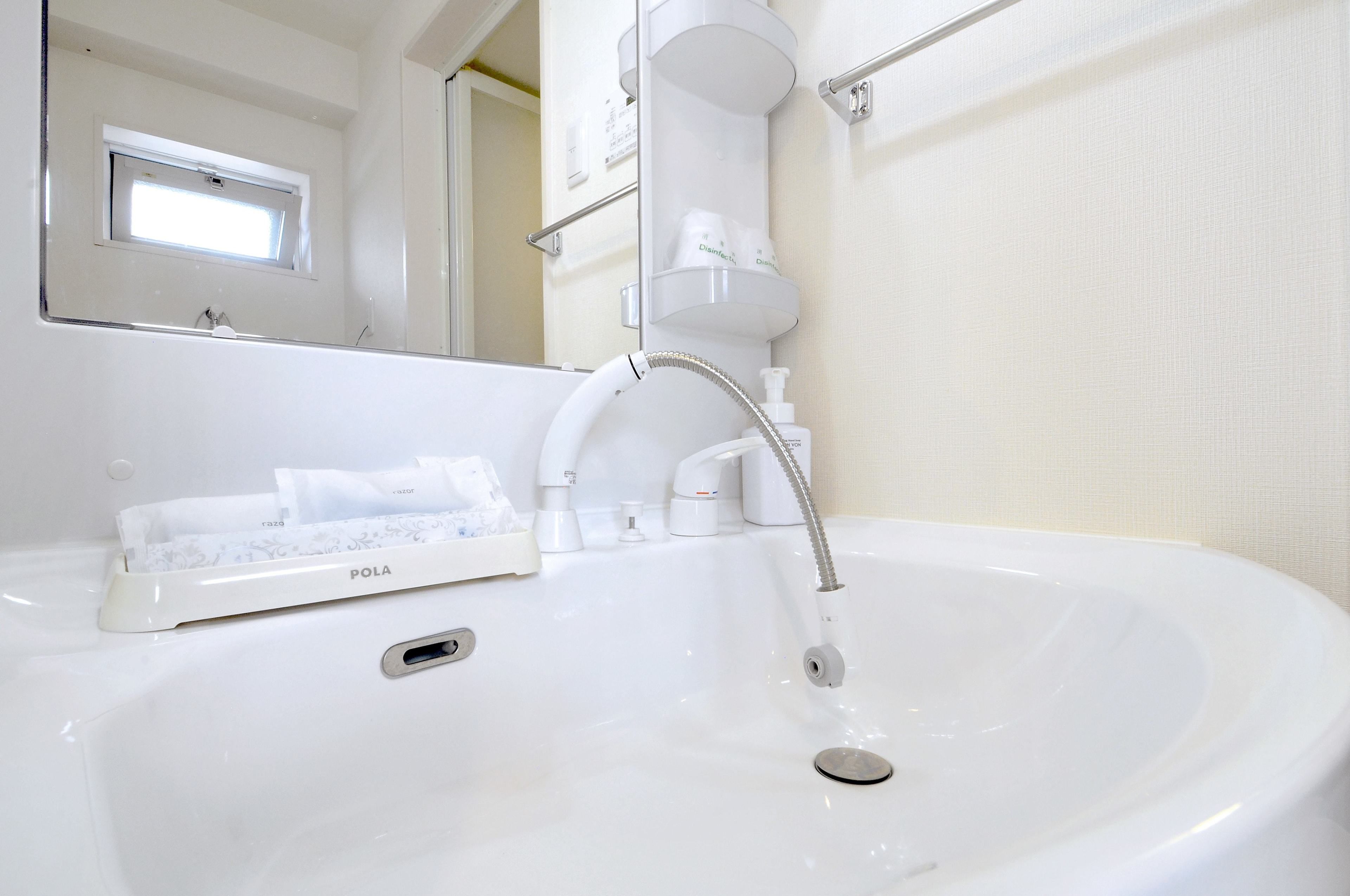 A white bathroom sink with a modern faucet, a mirror above it, and a window above the mirror.
