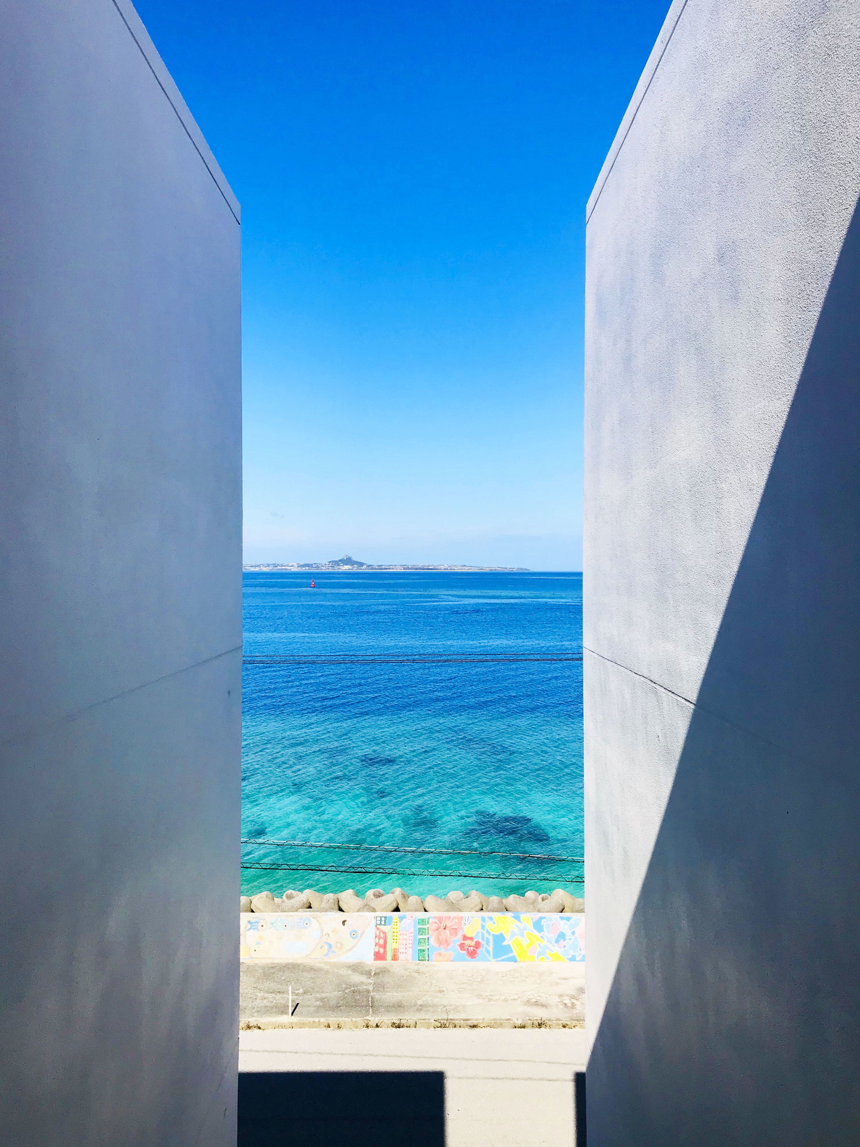 A view through a concrete structure to a turquoise sea with a distant landmass and colorful artwork on the ground.