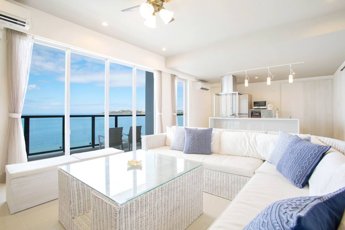 A modern living room with a glass coffee table, white sofa, and a view of the sea.