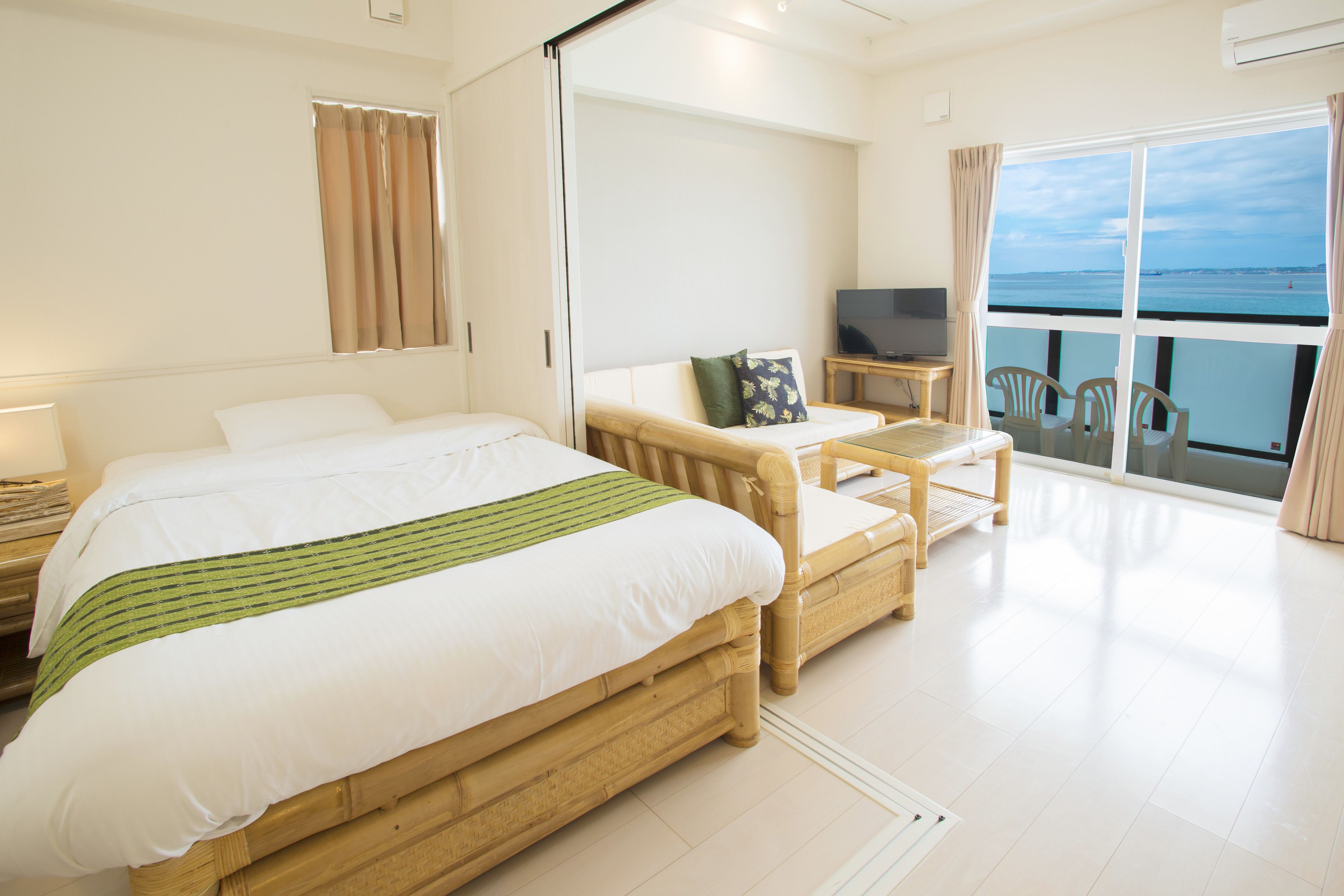 A hotel room with a large bed, a sofa, a TV, and a balcony with a view.