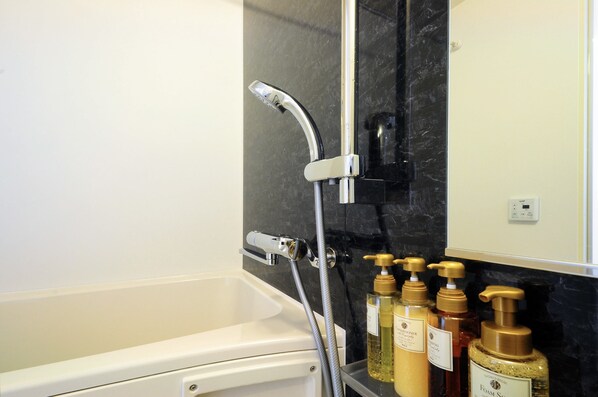 A bathroom with a white bathtub, a shower with a chrome faucet, and three bottles of shampoo on the counter. - Costa Bella Condominiun Resort (Motobu)