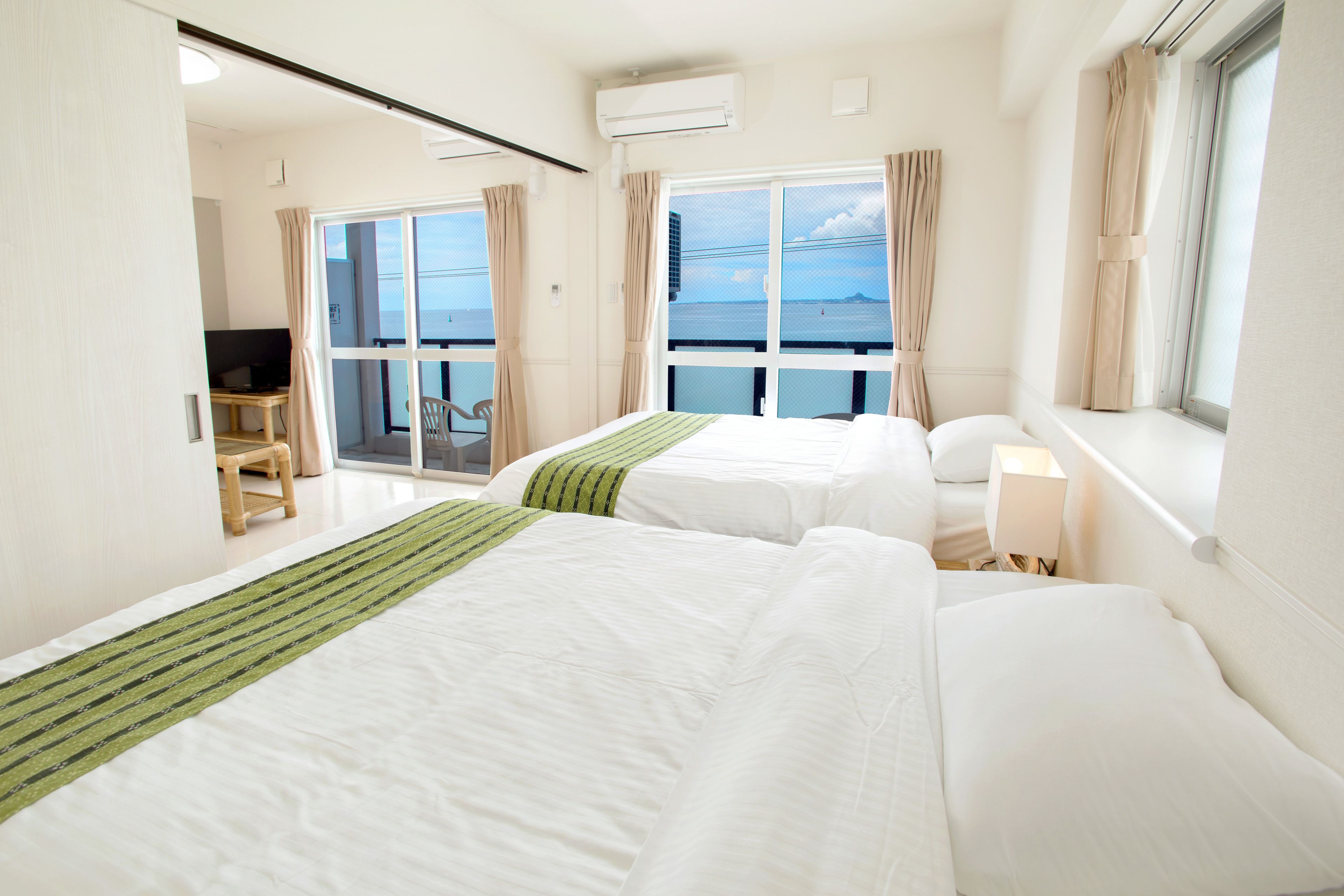 A hotel room with two beds, a desk, a chair, and a view of the sea.
