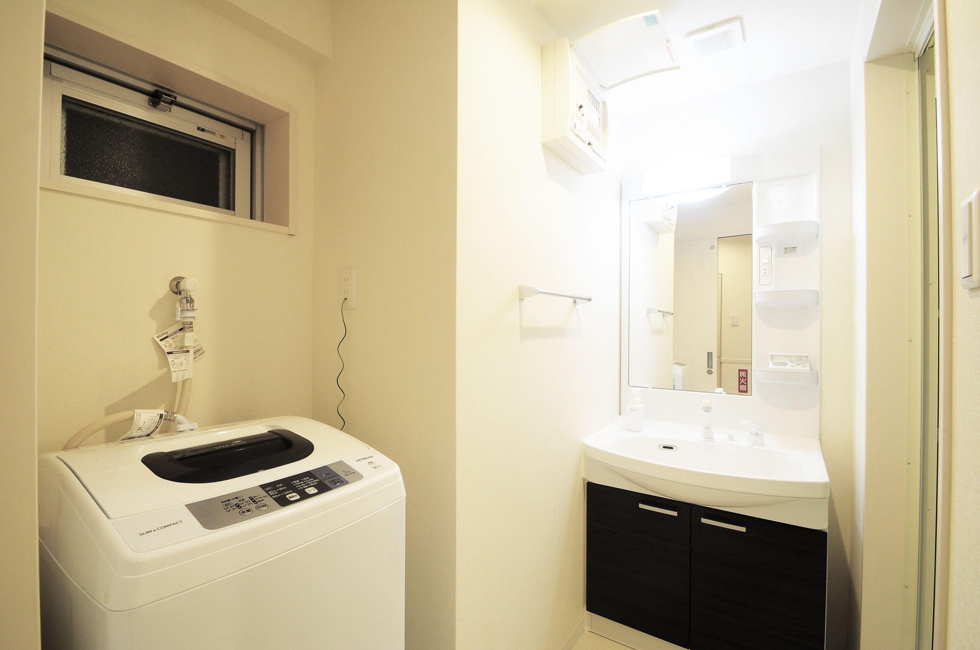 A compact bathroom with a washing machine, a sink, and a mirror.