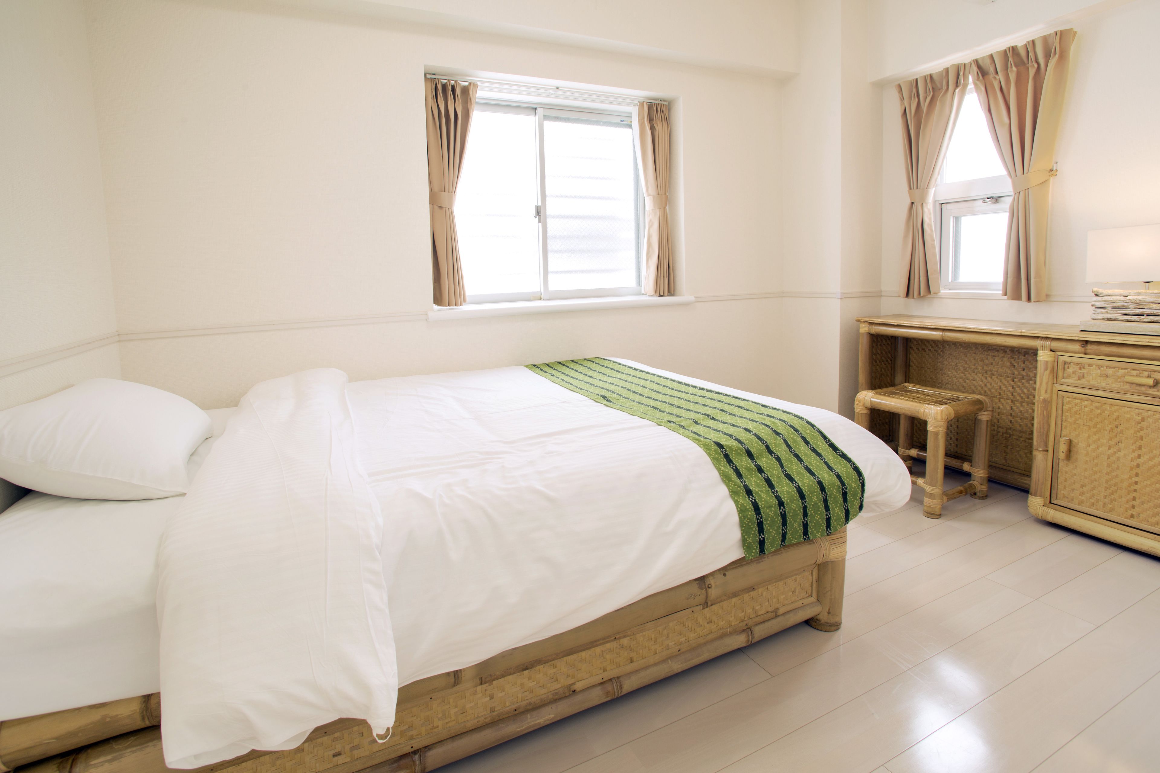 Une chambre à coucher avec un lit, une fenêtre, un petit tabouret et une armoire en bois.