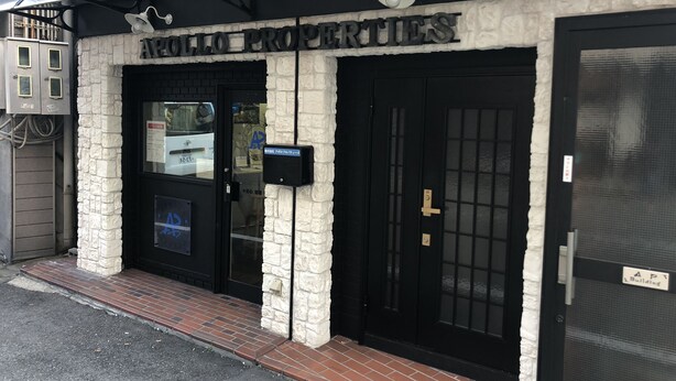 Un edificio con fachada blanco y negro, un cartel que dice "APOLLO PROPERTIES" y una puerta negra con un ventanal encima.
