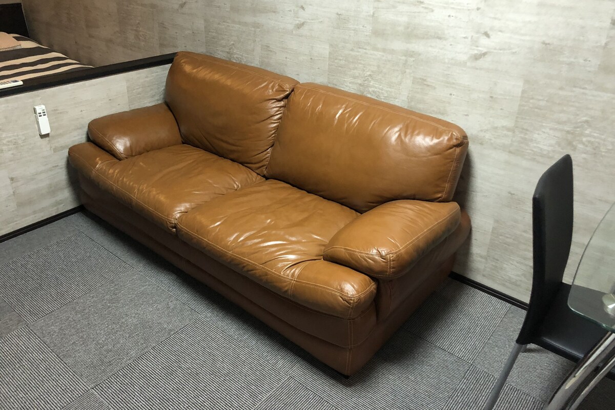 A brown leather sofa in a room with a concrete wall and a gray carpet.