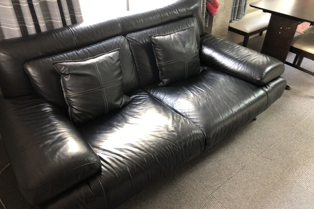A black leather sofa with two cushions, a wooden table, and a chair in a room with striped curtains.