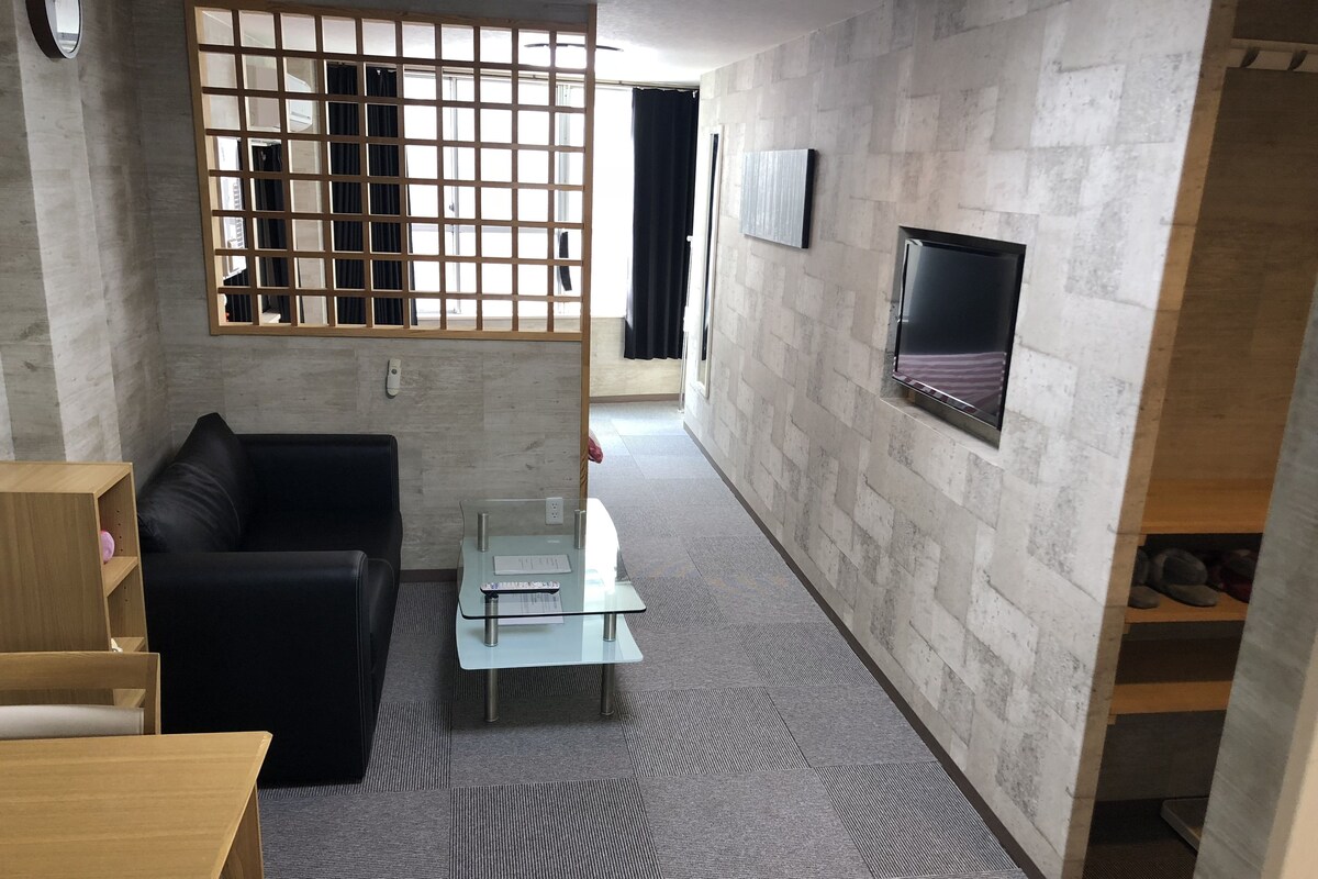 A modern living room with a black leather sofa, a glass coffee table, a wooden TV stand, and a patterned carpet.