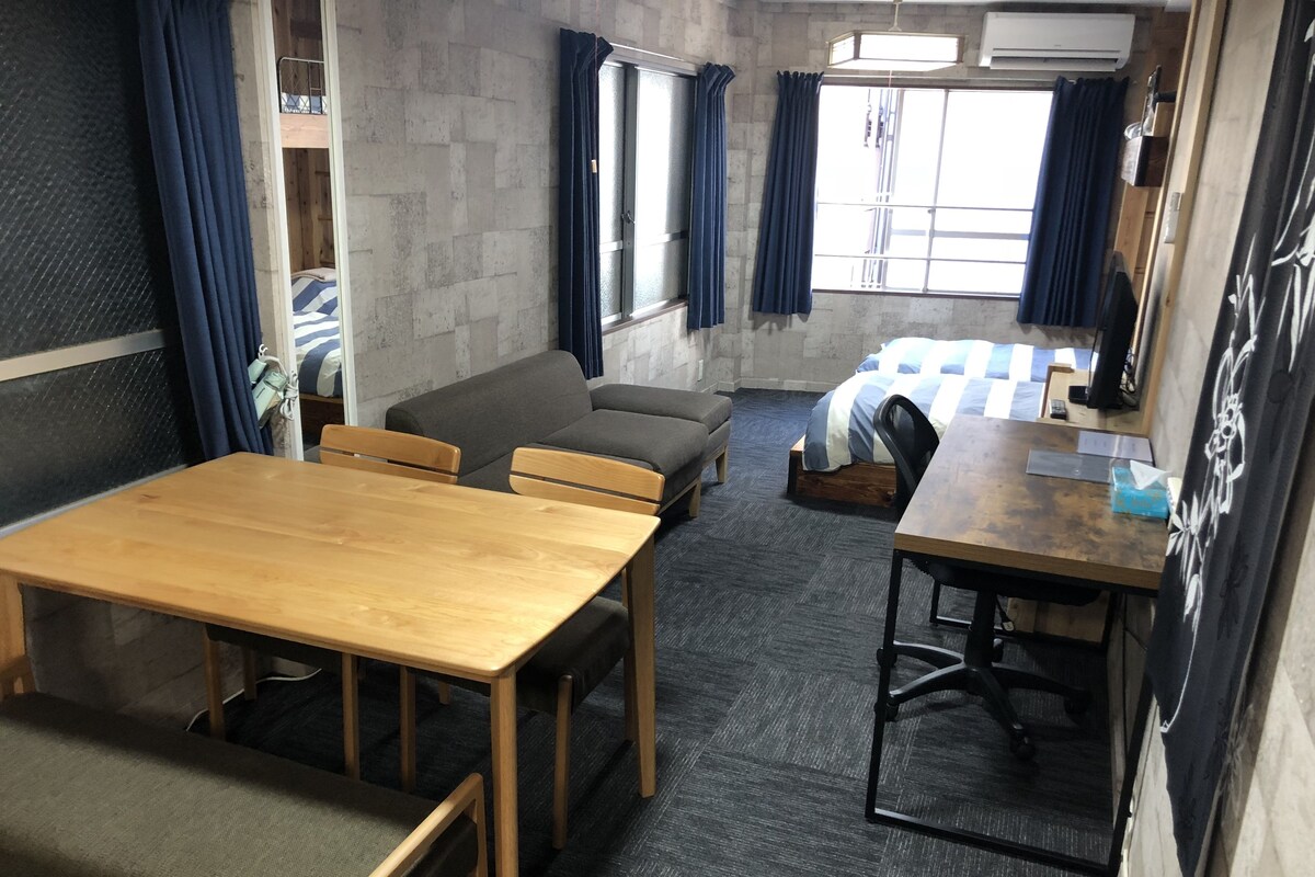 A room with a wooden table, two sofas, a bunk bed, and a bunk chair.