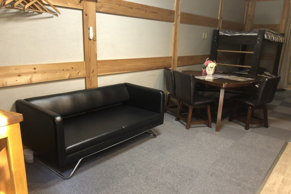 A room with a black sofa, wooden dining table, and chairs.