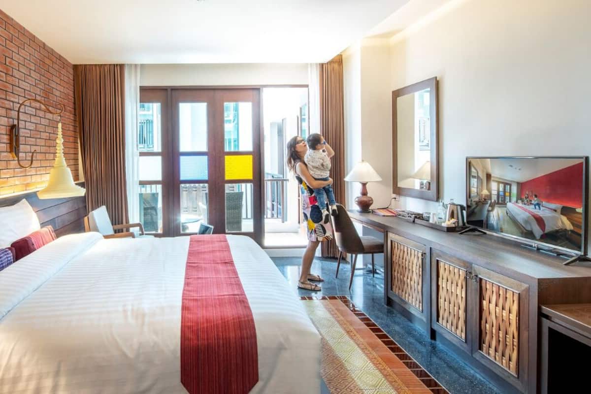 Quarto de hotel com uma cama grande, uma mesa de trabalho com uma TV, uma parede de tijolos e vista para a cidade.