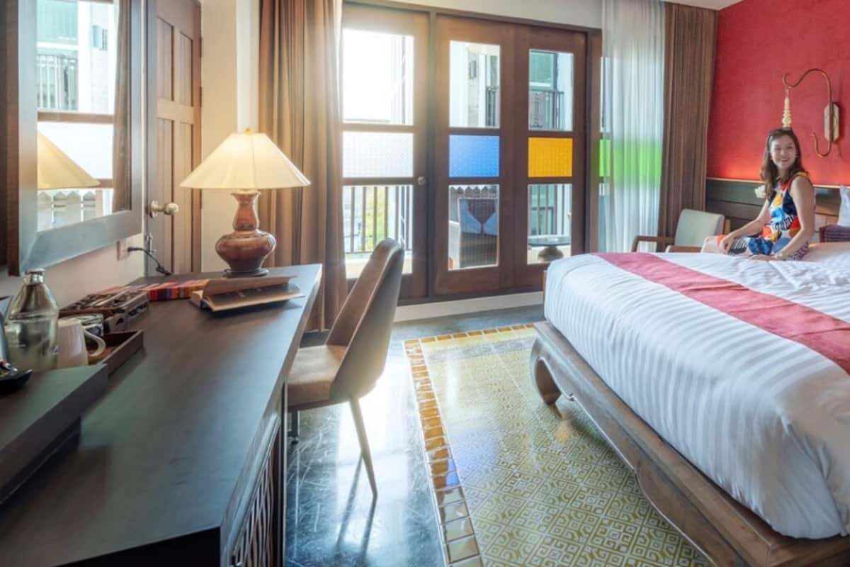 Quarto de hotel com cama, escrivaninha, luminária e janela com vista.